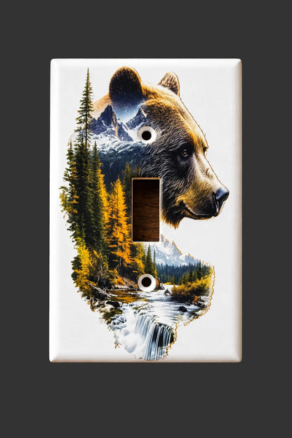 A white single-toggle light switch plate cover featuring a printed design of a bear's head layered over a forest and waterfall landscape, shown standing on a dark surface.