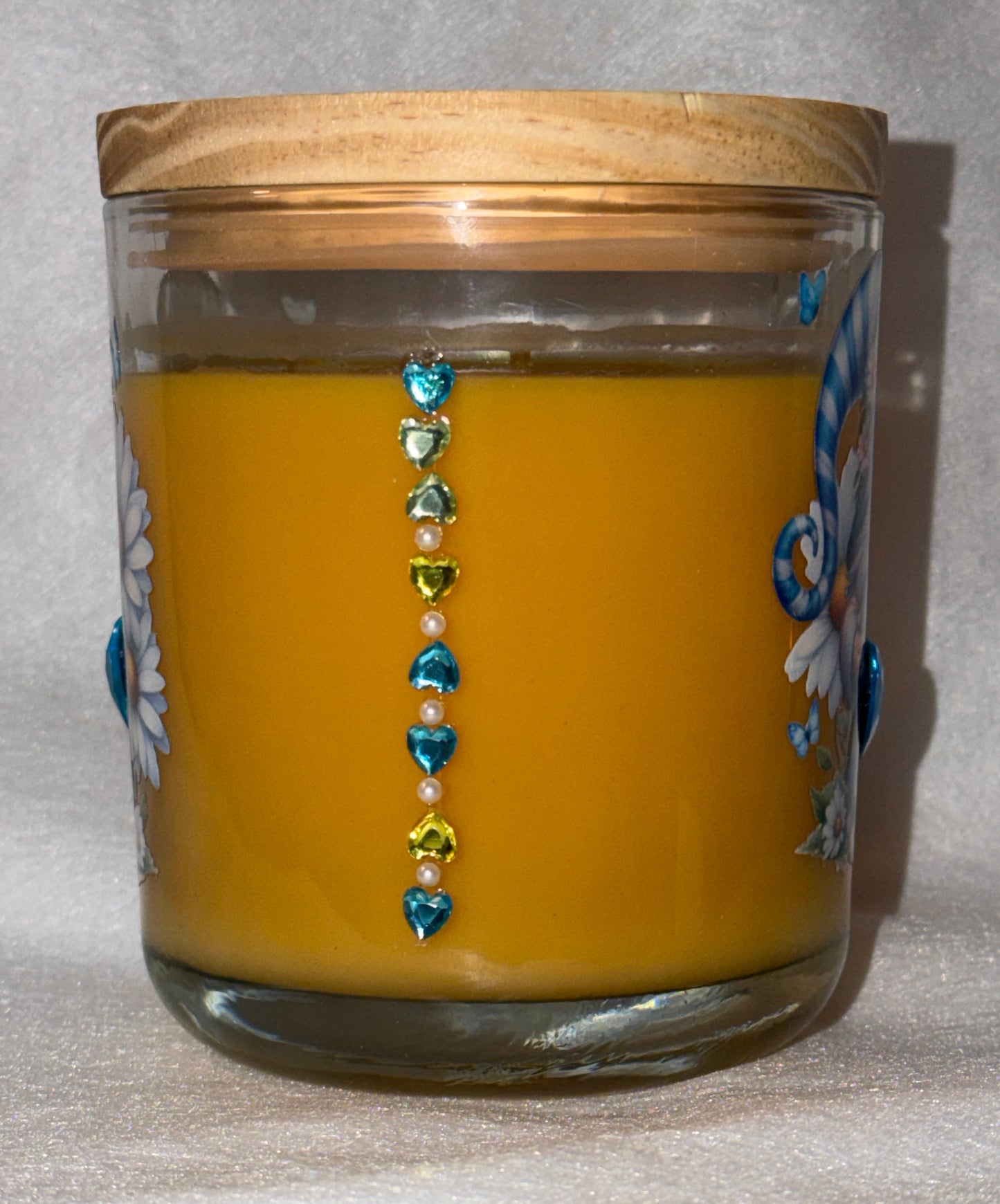 Yellow candle in a glass jar with decorative beads on a textured surface
