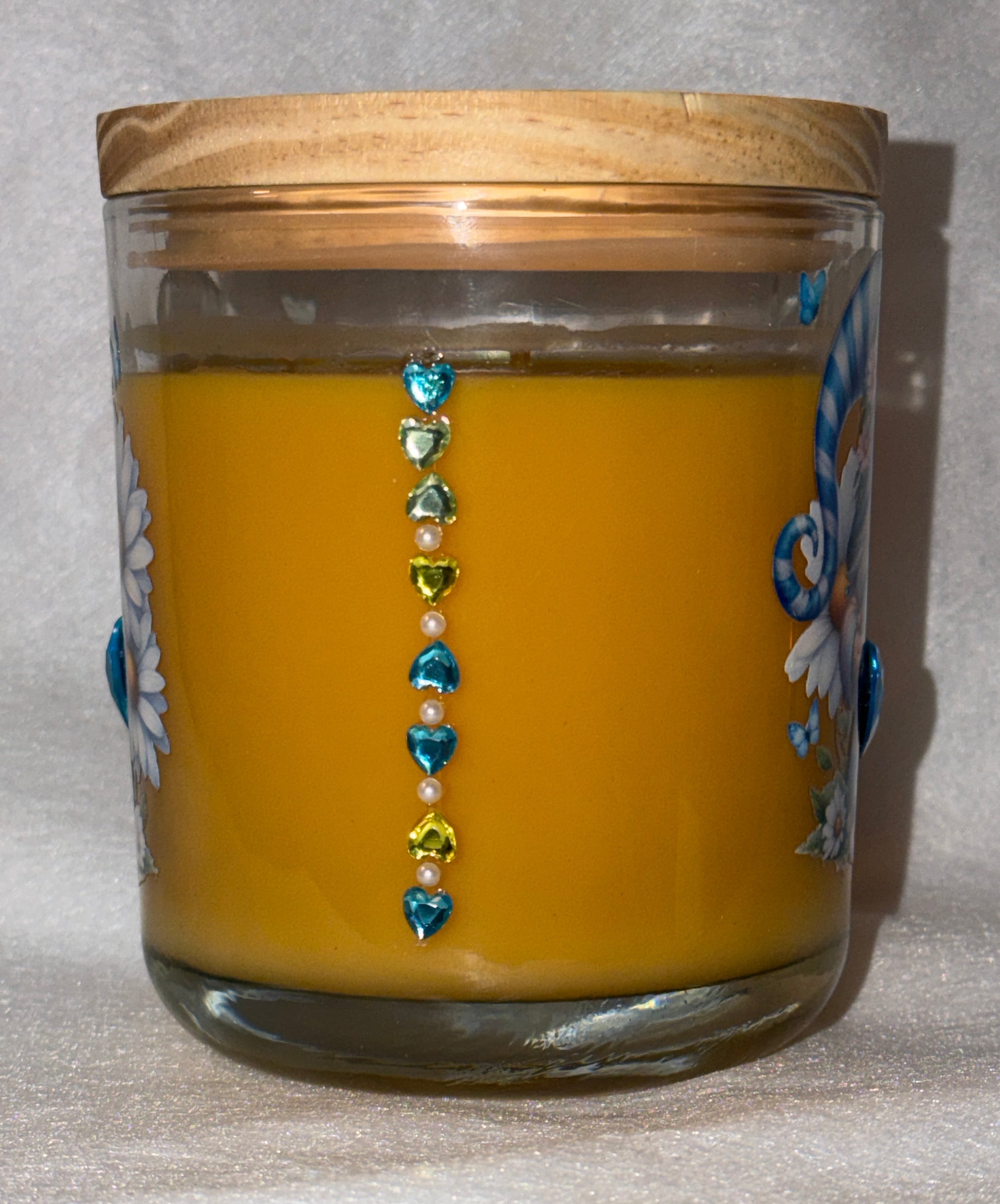 Yellow candle in a glass jar with decorative beads on a textured surface