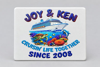 A rectangular white metal license plate featuring a colorful custom design. The design includes the text 'JOY & KEN' at the top in purple letters, an illustration of a cruise ship above an underwater reef scene with a turtle and coral, the phrase 'CRUISING LIFE TOGETHER SINCE 2008' in blue and teal lettering, and a silver border.